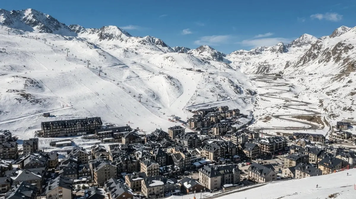 Hotels and shops of Pas de la Casa below open snowy slopes with ski lifts and a road climbing toward the pass